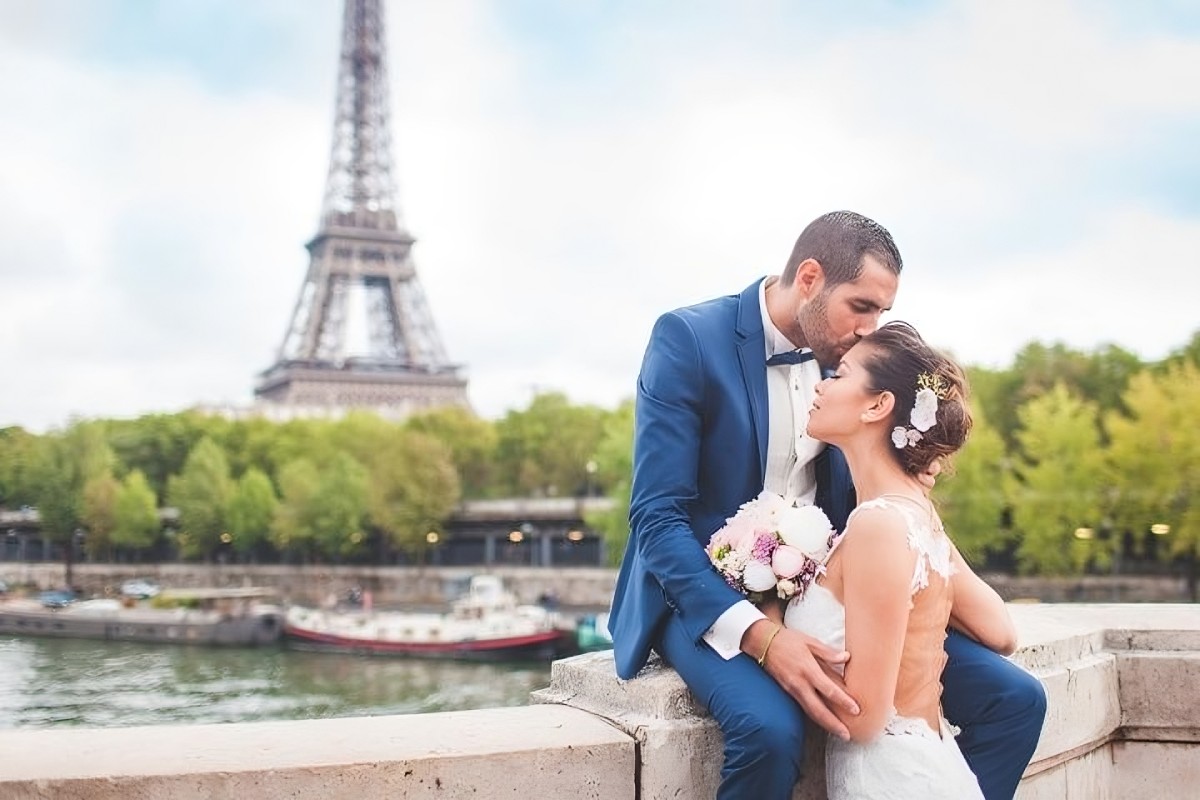 Marié embrassant tendrement sa femme en robe blanche devant la Tour Eiffel, symbole romantique du mariage traditionnel à la française.